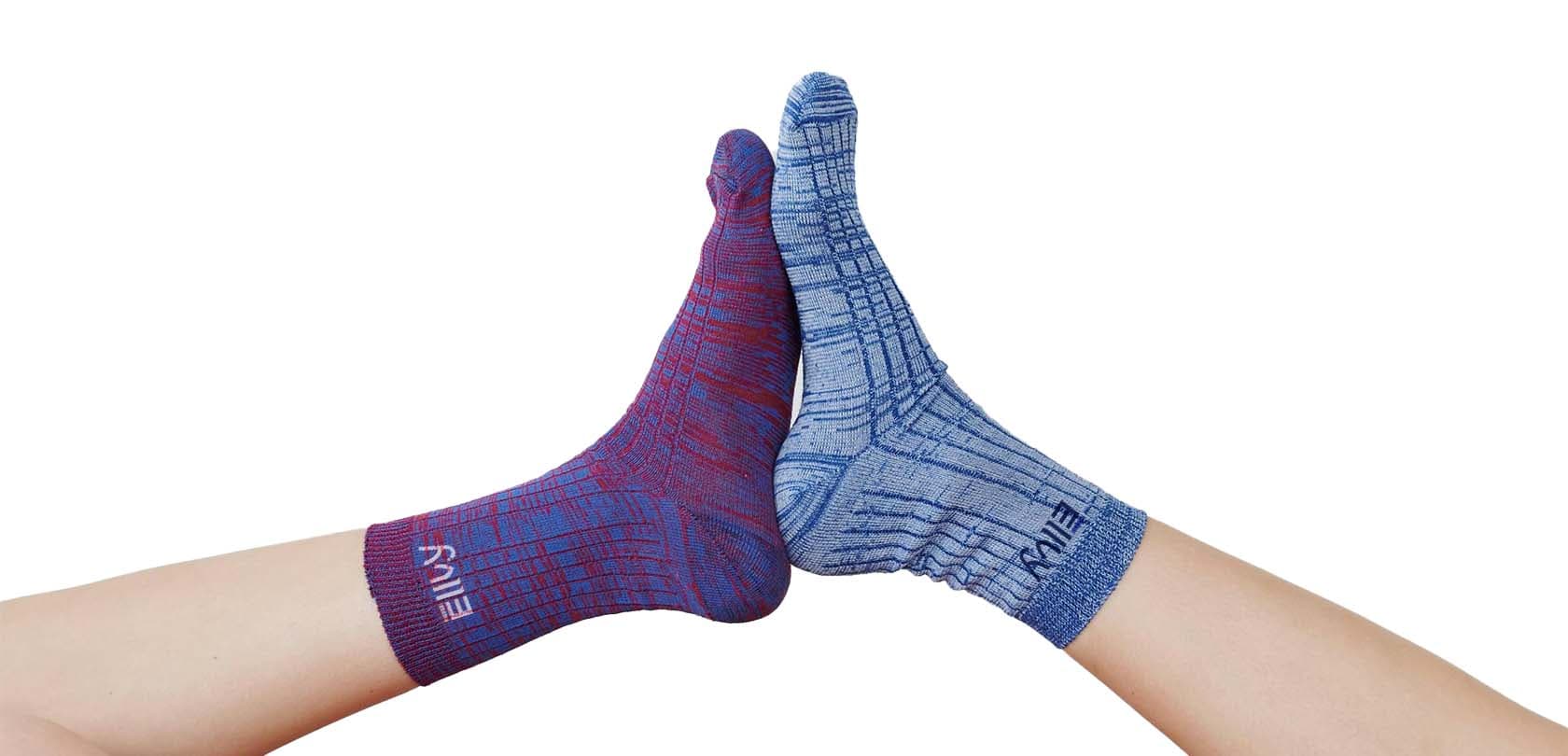 Two crossed feet wearing heathered crew socks in maroon and light blue, each with the ELLVY logo on the cuff